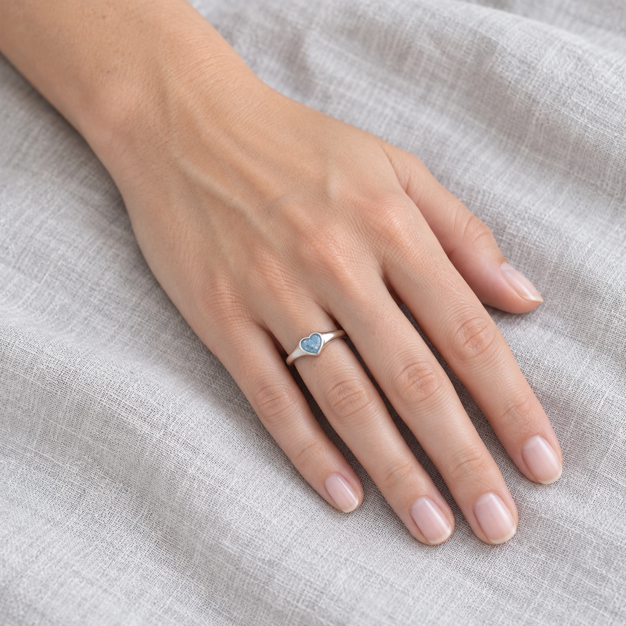 Petite Heart Ashes Ring worn on a hand, with its plain tapered silver band