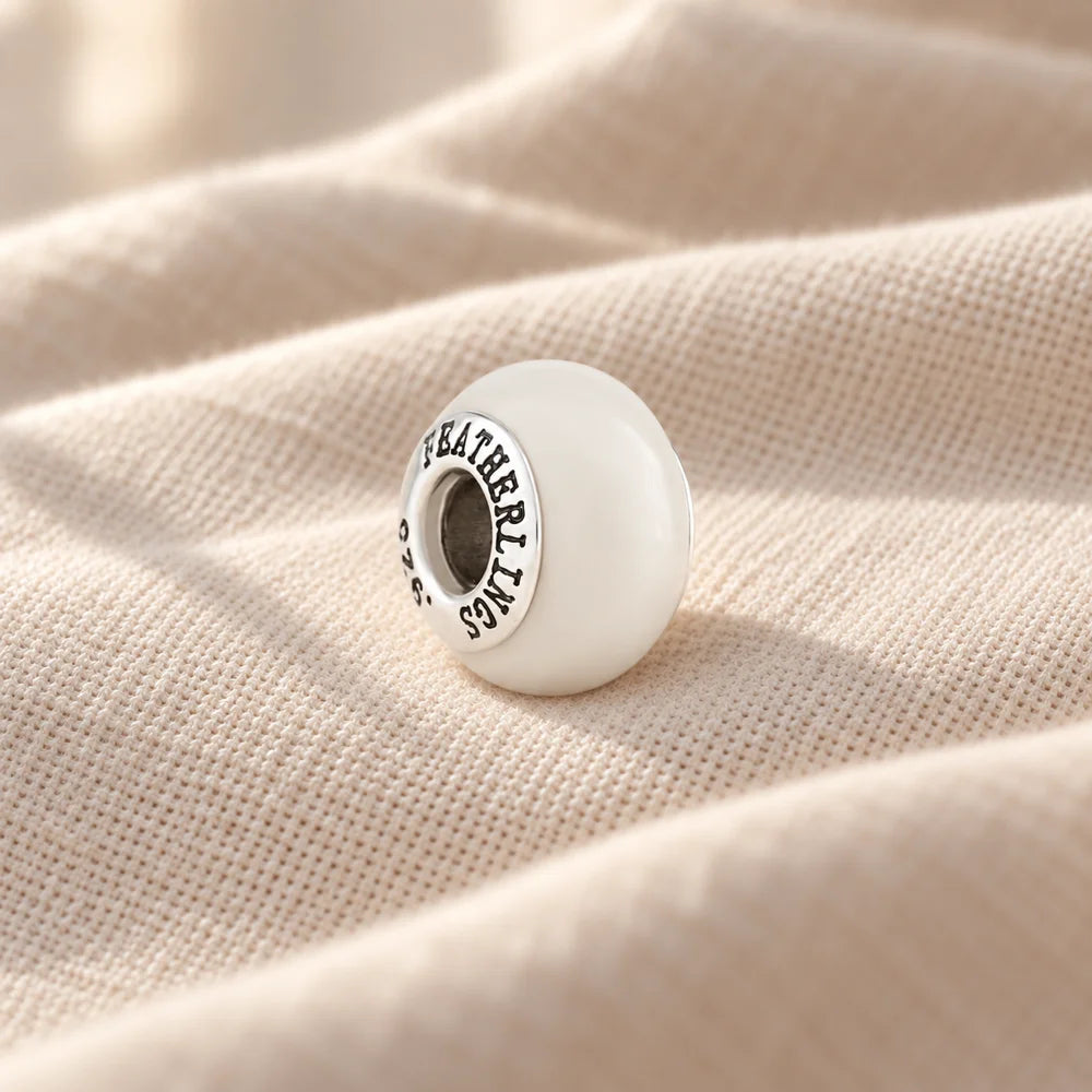 Round breast milk charm with a sterling silver core on pale linen — illustrative preview